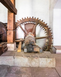 Schloss und Schlossgarten Schwetzingen - Sonstige Bauten - Oberes Wasserwerk - Pumpenstube - Von innen - Westliche Räder und Pumpen - Von Norden - Blick auf das Holzrad im Inneren der Stube, das mit dem westlichen Wasserrad verbunden ist; Holzrad: mit Holzzähnen im Radreifen, Durchmesser ca. 2,6 Meter; Welle im Holzrad: Durchmesser ca. 0,5 Meter, Länge ca. 6,5 Meter; das südliche Ende der Welle lagert in einer Nische an der Nordwand des Kellereigebäudes (im Hintergrund hinter dem Gitter etwas zu sehen); das mittige Holzrad greift links in ein weiteres Holzrad ein, das mit der Kurbelwelle der westlichen Pumpen verbunden ist; linkes Holzrad: Durchmesser ca. 1,8 Meter, mit zwei Radreifen, verbunden im Abstand von ca. 70 Zentimeter mit hölzernen Rundstäbe (Gesamte Anlage Brunnenstube, Pumpenstube, Räderwerk, Wasserturm und Kühlhaus): Länge x Breite: ca. 30 x 29 Meter, Pumpenstube: Länge x Breite: ca. 13 x 9 Meter; Bauzeit Anlage: um 1774, Gesamtinstandsetzung: 1994–2000; Architekt: Nicolas de Pigage, Brunnenmeister: Thomas Breuer) (aufgenommen im Juli 2025, am Nachmittag) Schloss und Schlossgarten Schwetzingen - Sonstige Bauten - Oberes Wasserwerk - Pumpenstube - Von innen - Westliche Räder und Pumpen - Von Norden - Blick auf das Holzrad im Inneren der Stube, das mit dem westlichen Wasserrad verbunden ist; Holzrad: mit Holzzähnen im Radreifen, Durchmesser ca. 2,6 Meter; Welle im Holzrad: Durchmesser ca. 0,5 Meter, Länge ca. 6,5 Meter; das südliche Ende der Welle lagert in einer Nische an der Nordwand des Kellereigebäudes (im Hintergrund hinter dem Gitter etwas zu sehen); das mittige Holzrad greift links in ein weiteres Holzrad ein, das mit der Kurbelwelle der westlichen Pumpen verbunden ist; linkes Holzrad: Durchmesser ca. 1,8 Meter, mit zwei Radreifen, verbunden im Abstand von ca. 70 Zentimeter mit hölzernen Rundstäbe (Gesamte Anlage Brunnenstube, Pumpenstube, Räderwerk, Wasserturm und Kühlhaus): Länge x Breite: ca. 30 x 29 Meter, Pumpenstube: Länge x Breite: ca. 13 x 9 Meter; Bauzeit Anlage: um 1774, Gesamtinstandsetzung: 1994–2000; Architekt: Nicolas de Pigage, Brunnenmeister: Thomas Breuer) (aufgenommen im Juli 2025, am Nachmittag)
