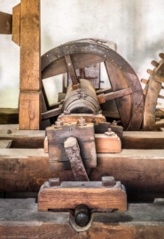 Schloss und Schlossgarten Schwetzingen - Sonstige Bauten - Oberes Wasserwerk - Pumpenstube - Von innen - Westliche Räder und Pumpen - Von Norden - Blick auf den westlichen Pumpenschacht, eingerahmt von vier Balken, darüber ein Querbalken in der Mitte (vorne), darüber die Kurbelwelle (vorne oben), dahinter die mit der Kurbelwelle verbundene Holzwelle (Mitte) sowie das Holzrad (hinten); Pumpenschacht: Länge x Breite x Tiefe ca. 2,5 x 2 x 4 Meter; Kurbelwelle: aus Metall, für vier Kolbenstangen bzw. Kolben; Welle: Durchmesser ca. 0,5 Meter; Holzrad: Durchmesser ca. 1,8 Meter, mit zwei Radreifen, verbunden im Abstand von ca. 70 Zentimeter mit hölzernen Rundstäbe; das mittige Holzrad greift rechts in ein weiteres Holzrad ein, das mit dem westlichen Wasserrad verbunden ist; rechtes Holzrad: mit Holzzähnen im Radreifen, Durchmesser ca. 2,6 Meter (Gesamte Anlage Brunnenstube, Pumpenstube, Räderwerk, Wasserturm und Kühlhaus): Länge x Breite: ca. 30 x 29 Meter, Pumpenstube: Länge x Breite: ca. 13 x 9 Meter; Bauzeit Anlage: um 1774, Gesamtinstandsetzung: 1994–2000; Architekt: Nicolas de Pigage, Brunnenmeister: Thomas Breuer) (aufgenommen im Juli 2025, am Nachmittag) Schloss und Schlossgarten Schwetzingen - Sonstige Bauten - Oberes Wasserwerk - Pumpenstube - Von innen - Westliche Räder und Pumpen - Von Norden - Blick auf den westlichen Pumpenschacht, eingerahmt von vier Balken, darüber ein Querbalken in der Mitte (vorne), darüber die Kurbelwelle (vorne oben), dahinter die mit der Kurbelwelle verbundene Holzwelle (Mitte) sowie das Holzrad (hinten); Pumpenschacht: Länge x Breite x Tiefe ca. 2,5 x 2 x 4 Meter; Kurbelwelle: aus Metall, für vier Kolbenstangen bzw. Kolben; Welle: Durchmesser ca. 0,5 Meter; Holzrad: Durchmesser ca. 1,8 Meter, mit zwei Radreifen, verbunden im Abstand von ca. 70 Zentimeter mit hölzernen Rundstäbe; das mittige Holzrad greift rechts in ein weiteres Holzrad ein, das mit dem westlichen Wasserrad verbunden ist; rechtes Holzrad: mit Holzzähnen im Radreifen, Durchmesser ca. 2,6 Meter (Gesamte Anlage Brunnenstube, Pumpenstube, Räderwerk, Wasserturm und Kühlhaus): Länge x Breite: ca. 30 x 29 Meter, Pumpenstube: Länge x Breite: ca. 13 x 9 Meter; Bauzeit Anlage: um 1774, Gesamtinstandsetzung: 1994–2000; Architekt: Nicolas de Pigage, Brunnenmeister: Thomas Breuer) (aufgenommen im Juli 2025, am Nachmittag)