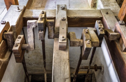 Schloss und Schlossgarten Schwetzingen - Sonstige Bauten - Oberes Wasserwerk - Pumpenstube - Von innen - Westliche Räder und Pumpen - Von Westen - Blick schräg nach unten in den westlichen Pumpenschacht (Länge x Breite x Tiefe ca. 2,5 x 2 x 4 Meter), auf die Kurbelwelle für die vier Hubkolbenpumpen und auf die vier Kolbenstangen (Länge ca. 2,9 Meter) (Gesamte Anlage Brunnenstube, Pumpenstube, Räderwerk, Wasserturm und Kühlhaus): Länge x Breite: ca. 30 x 29 Meter, Pumpenstube: Länge x Breite: ca. 13 x 9 Meter; Bauzeit Anlage: um 1774, Gesamtinstandsetzung: 1994–2000; Architekt: Nicolas de Pigage, Brunnenmeister: Thomas Breuer) (aufgenommen im Juli 2025, am späten Nachmittag)