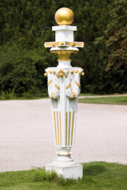 Schloss und Schlossgarten Schwetzingen - Garten - Zwischen Angloisen & Bosketten / Kugelallee - 8 Postamente mit Kugeln - Von Südost - Blick auf eines der acht Postamente mit vergoldeten Kugeln; Standort: im Nordwesten des Rasenfeldes; oben eine vergoldete Kugel, darunter eine Platte mit goldenen Rosetten und Kügelchen, darunter ein Kapitell aus Akanthusblättern, darunter ein sich nach unten verjüngender Pfeiler, geschmückt mit (teilweise vergoldeten) Kanneluren, am oberen Ende mit vergoldeten Kügelchen und Stiften, an denen Lorbeergirlanden angebracht sind; ganz unten ein profilierter Fuß, verziert mit einem Flechtring, darunter ein quadratisches Fußgestell (Bildhauer: der Werkstatt von Franz Conrad Linck (1730-1793) zugeschrieben; Datierung: um 1770; Material: Sandstein, weiß gefasst; Höhe Gesamt / Sockel: 276 / 33 Zentimeter; Inv.Nr. G 4221-4228; Kopie, Original im Depot) (aufgenommen im Juli 2025, um die Mittagszeit)