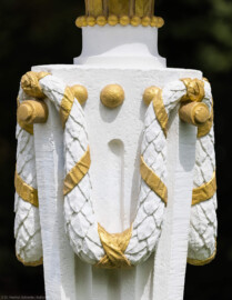 Schloss und Schlossgarten Schwetzingen - Garten - Zwischen Angloisen & Bosketten / Kugelallee - 8 Postamente mit Kugeln - Von Südost - Blick auf Details eines der acht Postamente mit vergoldeten Kugeln; Standort: im Nordwesten des Rasenfeldes; oben ein Kapitell aus Akanthusblättern, darunter ein sich nach unten verjüngender Pfeiler, geschmückt mit Kanneluren, am oberen Ende mit vergoldeten Kügelchen und Stiften, an denen Lorbeergirlanden angebracht sind (Bildhauer: der Werkstatt von Franz Conrad Linck (1730-1793) zugeschrieben; Datierung: um 1770; Material: Sandstein, weiß gefasst; Höhe Gesamt / Sockel: 276 / 33 Zentimeter; Inv.Nr. G 4221-4228; Kopie, Original im Depot) (aufgenommen im Juli 2025, um die Mittagszeit) Schloss und Schlossgarten Schwetzingen - Garten - Zwischen Angloisen & Bosketten / Kugelallee - 8 Postamente mit Kugeln - Von Südost - Blick auf Details eines der acht Postamente mit vergoldeten Kugeln; Standort: im Nordwesten des Rasenfeldes; oben ein Kapitell aus Akanthusblättern, darunter ein sich nach unten verjüngender Pfeiler, geschmückt mit Kanneluren, am oberen Ende mit vergoldeten Kügelchen und Stiften, an denen Lorbeergirlanden angebracht sind (Bildhauer: der Werkstatt von Franz Conrad Linck (1730-1793) zugeschrieben; Datierung: um 1770; Material: Sandstein, weiß gefasst; Höhe Gesamt / Sockel: 276 / 33 Zentimeter; Inv.Nr. G 4221-4228; Kopie, Original im Depot) (aufgenommen im Juli 2025, um die Mittagszeit)