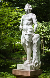 Schloss und Schlossgarten Schwetzingen - Garten - Um den Großen Weiher - Skulptur Rhetorica (ca. 80 Meter nordwestlich des Merkurtempels, "verborgen" in einer Baum-/Buschgruppe) - Von Osten - Blick auf die allegorische Figur "Rhetorica", daneben ein Bienenkorb auf einem Baumstumpf (Bildhauer: Peter van den Branden (†1720) zugeschrieben; Datierung: unbekannt) (aufgenommen im Juli 2025, am frühen Nachmittag)