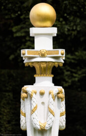 Schloss und Schlossgarten Schwetzingen - Garten - Zwischen Angloisen & Bosketten / Kugelallee - 8 Postamente mit Kugeln - Von Südost - Blick auf Details eines der acht Postamente mit vergoldeten Kugeln; Standort: im Nordwesten des Rasenfeldes; oben eine vergoldete Kugel, darunter eine Platte mit goldenen Rosetten und Kügelchen, darunter ein Kapitell aus Akanthusblättern, darunter ein sich nach unten verjüngender Pfeiler, geschmückt mit Kanneluren, am oberen Ende mit vergoldeten Kügelchen und Stiften, an denen Lorbeergirlanden angebracht sind (Bildhauer: der Werkstatt von Franz Conrad Linck (1730-1793) zugeschrieben; Datierung: um 1770; Material: Sandstein, weiß gefasst; Höhe Gesamt / Sockel: 276 / 33 Zentimeter; Inv.Nr. G 4221-4228; Kopie, Original im Depot) (aufgenommen im Juli 2025, um die Mittagszeit)