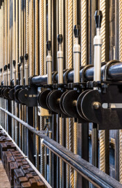 Schloss und Schlossgarten Schwetzingen - Garten - Schlosstheater - Von innen - Bühnenraum, südliche Arbeitsgalerie - Von Nordwest - Blick vom westlichen Ende der südlichen Arbeitsgalerie (Höhe ca. 8 Meter) auf die Feststellvorrichtungen der Züge, mit denen die Kommandoseile der Handkonterzüge festgeklemmt werden können, um die Lasten in bestimmten Positionen halten zu können; unten im Bild lagern Kontergewichte der Handkonterzüge auf der Arbeitsgalerie (Gesamter Bau: Länge x Breite: ca. 62 x 35 Meter; Architekt: Nicolas de Pigage (1723-1796); Bauzeit: 1752-1753, Erweiterung 1762, Sanierung: 1937, Renovierung: 1952, Generalsanierung / Umbau 1971-1974, Restaurierung: 1999-2005) (aufgenommen im Juli 2025, am Nachmittag) Schloss und Schlossgarten Schwetzingen - Garten - Schlosstheater - Von innen - Bühnenraum, südliche Arbeitsgalerie - Von Nordwest - Blick vom westlichen Ende der südlichen Arbeitsgalerie (Höhe ca. 8 Meter) auf die Feststellvorrichtungen der Züge, mit denen die Kommandoseile der Handkonterzüge festgeklemmt werden können, um die Lasten in bestimmten Positionen halten zu können; unten im Bild lagern Kontergewichte der Handkonterzüge auf der Arbeitsgalerie (Gesamter Bau: Länge x Breite: ca. 62 x 35 Meter; Architekt: Nicolas de Pigage (1723-1796); Bauzeit: 1752-1753, Erweiterung 1762, Sanierung: 1937, Renovierung: 1952, Generalsanierung / Umbau 1971-1974, Restaurierung: 1999-2005) (aufgenommen im Juli 2025, am Nachmittag)