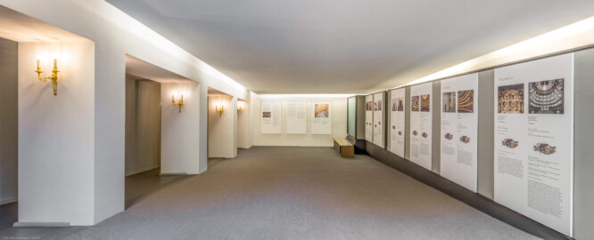Schloss und Schlossgarten Schwetzingen - Garten - Schlosstheater - Von innen - 1. Obergeschoss (Balkon), nördliches Foyer - Von Osten - Blick nach Westen in das nördliche Foyer im 1. Obergeschoss; links (südlich) hinter den Pfeilern die Zugänge zu den Rängen; mittig und rechts Tafeln einer Ausstellung zu den kurfürstlichen Opern, der kurfürstlichen Hofmusik, den Reisen Mozarts durch Europa sowie zu einigen Mozarttheatern (Gesamter Bau: Länge x Breite: ca. 62 x 35 Meter; Architekt: Nicolas de Pigage (1723-1796); Bauzeit: 1752-1753, Erweiterung 1762, Sanierung: 1937, Renovierung: 1952, Generalsanierung / Umbau 1971-1974, Restaurierung: 1999-2005) (aufgenommen im August 2025, am frühen Nachmittag)