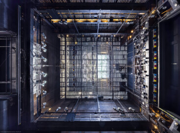 Schloss und Schlossgarten Schwetzingen - Garten - Schlosstheater - Von innen - Bühnenraum - Von Unten - Blick vom Zentrum des Bühnenbodens nach oben in den Bühnenraum; links ist Westen / die Hinterbühne, oben Süden / die Bühnenwand mit den vielen Zügen, rechts Osten / der Zuschauerraum, unten Norden / die Seitenbühne (mit geschlossenem Seitenbühnentor); der Rauchschieber (rechts der Bildmitte) auf dem Dach ist geöffnet, sodass Tageslicht auf die Wände und die Bühne fallen kann; im Bild oben, links und unten ist die begehbare Arbeitsgalerie (Höhe ca. 8 Meter) mit Scheinwerfern auf dem Geländer zu sehen, rechts die (in der Höhe einstellbare) begehbare Beleuchtungsbrücke mit umfangreicher Beleuchtungstechnik; das große Gitter in der Mitte ist der begehbare Rollenboden / Schnürboden (Höhe ca. 13,5 Meter), unter dem sich Zugstangen für Bühnenprospekte, Beleuchtung etc. befinden; im Bild rechts in den Ecken oben und unten sind die beiden begehbaren Portaltürme teilweise zu sehen (Gesamter Bau: Länge x Breite: ca. 62 x 35 Meter; Architekt: Nicolas de Pigage (1723-1796); Bauzeit: 1752-1753, Erweiterung 1762, Sanierung: 1937, Renovierung: 1952, Generalsanierung / Umbau 1971-1974, Restaurierung: 1999-2005) (aufgenommen im August 2025, am späten Vormittag) Schloss und Schlossgarten Schwetzingen - Garten - Schlosstheater - Von innen - Bühnenraum - Von Unten - Blick vom Zentrum des Bühnenbodens nach oben in den Bühnenraum; links ist Westen / die Hinterbühne, oben Süden / die Bühnenwand mit den vielen Zügen, rechts Osten / der Zuschauerraum, unten Norden / die Seitenbühne (mit geschlossenem Seitenbühnentor); der Rauchschieber (rechts der Bildmitte) auf dem Dach ist geöffnet, sodass Tageslicht auf die Wände und die Bühne fallen kann; im Bild oben, links und unten ist die begehbare Arbeitsgalerie (Höhe ca. 8 Meter) mit Scheinwerfern auf dem Geländer zu sehen, rechts die (in der Höhe einstellbare) begehbare Beleuchtungsbrücke mit umfangreicher Beleuchtungstechnik; das große Gitter in der Mitte ist der begehbare Rollenboden / Schnürboden (Höhe ca. 13,5 Meter), unter dem sich Zugstangen für Bühnenprospekte, Beleuchtung etc. befinden; im Bild rechts in den Ecken oben und unten sind die beiden begehbaren Portaltürme teilweise zu sehen (Gesamter Bau: Länge x Breite: ca. 62 x 35 Meter; Architekt: Nicolas de Pigage (1723-1796); Bauzeit: 1752-1753, Erweiterung 1762, Sanierung: 1937, Renovierung: 1952, Generalsanierung / Umbau 1971-1974, Restaurierung: 1999-2005) (aufgenommen im August 2025, am späten Vormittag)