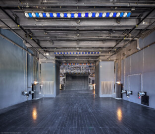 Schloss und Schlossgarten Schwetzingen - Garten - Schlosstheater - Von innen - Bühnenraum - Hinterbühne - Von Westen - Zentraler Blick vom großen mittleren Fenster der Westseite auf die Hinterbühne und im Hintergrund auf die Hauptbühne; die Vorhänge der drei Fenster der Westseite sind geöffnet, sodass viel Licht auf die Hinterbühne fällt; auch der Rauchschieber oberhalb der Hauptbühne auf dem Dach ist geöffnet, sodass Tageslicht auf die Hauptbühne fallen kann; links (Nordwand) und rechts (Südwand) befinden sich Handseilwinden mit Kurbeln (Traglast 300 kg) für die Höhenverstellung von Zugstangen an der Decke der Hinterbühne; im Hintergrund in der Bildmitte der geschlossene Eiserne Vorhang (Gesamter Bau: Länge x Breite: ca. 62 x 35 Meter; Architekt: Nicolas de Pigage (1723-1796); Bauzeit: 1752-1753, Erweiterung 1762, Sanierung: 1937, Renovierung: 1952, Generalsanierung / Umbau 1971-1974, Restaurierung: 1999-2005) (aufgenommen im August 2025, am frühen Nachmittag) Schloss und Schlossgarten Schwetzingen - Garten - Schlosstheater - Von innen - Bühnenraum - Hinterbühne - Von Westen - Zentraler Blick vom großen mittleren Fenster der Westseite auf die Hinterbühne und im Hintergrund auf die Hauptbühne; die Vorhänge der drei Fenster der Westseite sind geöffnet, sodass viel Licht auf die Hinterbühne fällt; auch der Rauchschieber oberhalb der Hauptbühne auf dem Dach ist geöffnet, sodass Tageslicht auf die Hauptbühne fallen kann; links (Nordwand) und rechts (Südwand) befinden sich Handseilwinden mit Kurbeln (Traglast 300 kg) für die Höhenverstellung von Zugstangen an der Decke der Hinterbühne; im Hintergrund in der Bildmitte der geschlossene Eiserne Vorhang (Gesamter Bau: Länge x Breite: ca. 62 x 35 Meter; Architekt: Nicolas de Pigage (1723-1796); Bauzeit: 1752-1753, Erweiterung 1762, Sanierung: 1937, Renovierung: 1952, Generalsanierung / Umbau 1971-1974, Restaurierung: 1999-2005) (aufgenommen im August 2025, am frühen Nachmittag)