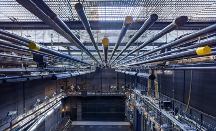 Schloss und Schlossgarten Schwetzingen - Garten - Schlosstheater - Von innen - Bühnenraum - Von Süden - Blick von der südlichen Gewichtsgalerie (Höhe ca. 11 Meter) nach Norden in den Bühnenraum und auf einige der ca. 55 Zugstangen unterhalb des Rollenbodens / Schnürbodens; der Rauchschieber (nicht sichtbar, oben, oberhalb der hellen Gitterfläche) auf dem Dach ist geöffnet, sodass Tageslicht auf den Rollenboden, die Gewichts- und Arbeitsgalerie sowie auf die Bühne fallen kann; das Gitter ganz oben ist der Boden des Rollenbodenss; links und mittig in halber Höhe die begehbare Arbeitsgalerie (Höhe ca. 8 Meter) mit Scheinwerfern auf dem Geländer; rechts in halber Höhe die (in der Höhe einstellbare) begehbare Beleuchtungsbrücke mit umfangreicher Beleuchtungstechnik; unten mittig das geschlossene Seitenbühnentor; unten rechts (unterhalb der Beleuchtungsbrücke) das geschlossene Eiserne Tor (Gesamter Bau: Länge x Breite: ca. 62 x 35 Meter; Architekt: Nicolas de Pigage (1723-1796); Bauzeit: 1752-1753, Erweiterung 1762, Sanierung: 1937, Renovierung: 1952, Generalsanierung / Umbau 1971-1974, Restaurierung: 1999-2005) (aufgenommen im August 2025, um die Mittagszeit) Schloss und Schlossgarten Schwetzingen - Garten - Schlosstheater - Von innen - Bühnenraum - Von Süden - Blick von der südlichen Gewichtsgalerie (Höhe ca. 11 Meter) nach Norden in den Bühnenraum und auf einige der ca. 55 Zugstangen unterhalb des Rollenbodens / Schnürbodens; der Rauchschieber (nicht sichtbar, oben, oberhalb der hellen Gitterfläche) auf dem Dach ist geöffnet, sodass Tageslicht auf den Rollenboden, die Gewichts- und Arbeitsgalerie sowie auf die Bühne fallen kann; das Gitter ganz oben ist der Boden des Rollenbodenss; links und mittig in halber Höhe die begehbare Arbeitsgalerie (Höhe ca. 8 Meter) mit Scheinwerfern auf dem Geländer; rechts in halber Höhe die (in der Höhe einstellbare) begehbare Beleuchtungsbrücke mit umfangreicher Beleuchtungstechnik; unten mittig das geschlossene Seitenbühnentor; unten rechts (unterhalb der Beleuchtungsbrücke) das geschlossene Eiserne Tor (Gesamter Bau: Länge x Breite: ca. 62 x 35 Meter; Architekt: Nicolas de Pigage (1723-1796); Bauzeit: 1752-1753, Erweiterung 1762, Sanierung: 1937, Renovierung: 1952, Generalsanierung / Umbau 1971-1974, Restaurierung: 1999-2005) (aufgenommen im August 2025, um die Mittagszeit)