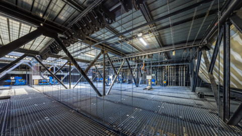 Schloss und Schlossgarten Schwetzingen - Garten - Schlosstheater - Von innen - Bühnenraum - Obermaschinerie - Rollenboden / Schnürboden - Von Nordwest - Blick nach Süden auf den Schnürboden (Höhe ca. 13,5 Meter); der Rauchschieber (nicht sichtbar, links, oberhalb der hellen Gitterfläche) auf dem Dach ist geöffnet, sodass Tageslicht auf den Rollenboden fallen kann; jede der ca. 55 Zugstangen unterhalb des Rollenbodens hängt an 4 Stahlseilen, die über Umlenkrollen (oben) mit den Gewichtsschlitten an der Südwand des Bühnenraums verbunden sind; rechts der Bildmitte stehen die 12 Elektro- und Elektro-Winden-Züge (Nutzlast meist ca. 500 kg); ganz links die Winde für den Rauchschieber (Nutzlast 500 kg, blau gefasst), rechts daneben die Winde für den Eisernen Vorhang (Nutzlast 500 kg, ebenso blau gefasst) (Gesamter Bau: Länge x Breite: ca. 62 x 35 Meter; Architekt: Nicolas de Pigage (1723-1796); Bauzeit: 1752-1753, Erweiterung 1762, Sanierung: 1937, Renovierung: 1952, Generalsanierung / Umbau 1971-1974, Restaurierung: 1999-2005) (aufgenommen im August 2025, am frühen Nachmittag) Schloss und Schlossgarten Schwetzingen - Garten - Schlosstheater - Von innen - Bühnenraum - Obermaschinerie - Rollenboden / Schnürboden - Von Nordwest - Blick nach Süden auf den Schnürboden (Höhe ca. 13,5 Meter); der Rauchschieber (nicht sichtbar, links, oberhalb der hellen Gitterfläche) auf dem Dach ist geöffnet, sodass Tageslicht auf den Rollenboden fallen kann; jede der ca. 55 Zugstangen unterhalb des Rollenbodens hängt an 4 Stahlseilen, die über Umlenkrollen (oben) mit den Gewichtsschlitten an der Südwand des Bühnenraums verbunden sind; rechts der Bildmitte stehen die 12 Elektro- und Elektro-Winden-Züge (Nutzlast meist ca. 500 kg); ganz links die Winde für den Rauchschieber (Nutzlast 500 kg, blau gefasst), rechts daneben die Winde für den Eisernen Vorhang (Nutzlast 500 kg, ebenso blau gefasst) (Gesamter Bau: Länge x Breite: ca. 62 x 35 Meter; Architekt: Nicolas de Pigage (1723-1796); Bauzeit: 1752-1753, Erweiterung 1762, Sanierung: 1937, Renovierung: 1952, Generalsanierung / Umbau 1971-1974, Restaurierung: 1999-2005) (aufgenommen im August 2025, am frühen Nachmittag)