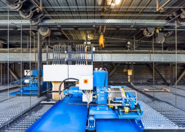 Schloss und Schlossgarten Schwetzingen - Garten - Schlosstheater - Von innen - Bühnenraum - Obermaschinerie - Rollenboden / Schnürboden - Von Westen - Blick auf die Ostwand; mittig die Winde für das Eiserne Tor (Nutzlast 500 kg; das Tor hängt an Gegengewichten), links davon eine Winde für den Rauchschieber (Nutzlast 500 kg); links und rechts Umlenkrollen und Stahlseile, die mit Zugstangen unterhalb des Rollenbodens verbunden sind (Gesamter Bau: Länge x Breite: ca. 62 x 35 Meter; Architekt: Nicolas de Pigage (1723-1796); Bauzeit: 1752-1753, Erweiterung 1762, Sanierung: 1937, Renovierung: 1952, Generalsanierung / Umbau 1971-1974, Restaurierung: 1999-2005) (aufgenommen im August 2025, am späten Vormittag) Schloss und Schlossgarten Schwetzingen - Garten - Schlosstheater - Von innen - Bühnenraum - Obermaschinerie - Rollenboden / Schnürboden - Von Westen - Blick auf die Ostwand; mittig die Winde für das Eiserne Tor (Nutzlast 500 kg; das Tor hängt an Gegengewichten), links davon eine Winde für den Rauchschieber (Nutzlast 500 kg); links und rechts Umlenkrollen und Stahlseile, die mit Zugstangen unterhalb des Rollenbodens verbunden sind (Gesamter Bau: Länge x Breite: ca. 62 x 35 Meter; Architekt: Nicolas de Pigage (1723-1796); Bauzeit: 1752-1753, Erweiterung 1762, Sanierung: 1937, Renovierung: 1952, Generalsanierung / Umbau 1971-1974, Restaurierung: 1999-2005) (aufgenommen im August 2025, am späten Vormittag)
