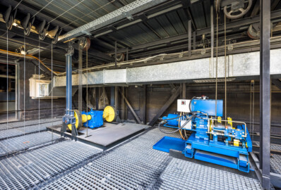 Schloss und Schlossgarten Schwetzingen - Garten - Schlosstheater - Von innen - Bühnenraum - Obermaschinerie - Rollenboden / Schnürboden - Von Südwest - Blick auf die Nordostecke des Rollenbodens; links der Antrieb für die in der Höhe einstellbare Beleuchtungsbrücke, rechts die Winde für den Rauchschieber (Nutzlast 500 kg); links Umlenkrollen und Stahlseile, die mit Zugstangen unterhalb des Rollenbodens verbunden sind; die Tür links führt in Technikräume (Gesamter Bau: Länge x Breite: ca. 62 x 35 Meter; Architekt: Nicolas de Pigage (1723-1796); Bauzeit: 1752-1753, Erweiterung 1762, Sanierung: 1937, Renovierung: 1952, Generalsanierung / Umbau 1971-1974, Restaurierung: 1999-2005) (aufgenommen im August 2025, am späten Vormittag) Schloss und Schlossgarten Schwetzingen - Garten - Schlosstheater - Von innen - Bühnenraum - Obermaschinerie - Rollenboden / Schnürboden - Von Südwest - Blick auf die Nordostecke des Rollenbodens; links der Antrieb für die in der Höhe einstellbare Beleuchtungsbrücke, rechts die Winde für den Rauchschieber (Nutzlast 500 kg); links Umlenkrollen und Stahlseile, die mit Zugstangen unterhalb des Rollenbodens verbunden sind; die Tür links führt in Technikräume (Gesamter Bau: Länge x Breite: ca. 62 x 35 Meter; Architekt: Nicolas de Pigage (1723-1796); Bauzeit: 1752-1753, Erweiterung 1762, Sanierung: 1937, Renovierung: 1952, Generalsanierung / Umbau 1971-1974, Restaurierung: 1999-2005) (aufgenommen im August 2025, am späten Vormittag)