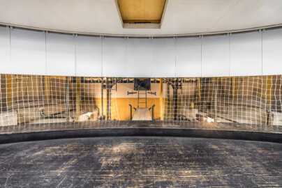 Schloss und Schlossgarten Schwetzingen - Garten - Schlosstheater - Von innen - Orchestergraben / Proszenium / Unterbühne - Von Westen - Blick vom Raum unterhalb der Vorbühne nach Osten in den Raum unterhalb des Proszeniumbodens; der Raum unter dem Proszenium beherbergt eine Hebevorrichtung für das Anheben und Absenken des Bodens des Proszeniums; im Moment ist der Boden teilweise abgesenkt; der runde Abschluss des Raums entspricht dem runden Abschluss der Vorbühne oberhalb; die grauen Platten oben verdecken die Sicht vom Zuschauerraum in die Unterbühne; hinter dem weißen Netz sind ganz links und ganz rechts die unteren Teile der Türen zum abgesenkten Orchestergraben etwas zu sehen; ganz oben eine herausnehmbare Platte für den Souffleurkasten auf der Vorbühne; die Holzbretter in der Bildmitte führen zu einer Leiter zum Abstieg in den Raum unterhalb des ganz abgesenkten Bodens; links und rechts hinter dem weißen Netz sind die vier Gewindespindeln zum Heben und Senken des Bodens des Proszeniums etwas zu sehen sehen (Gesamter Bau: Länge x Breite: ca. 62 x 35 Meter; Architekt: Nicolas de Pigage (1723-1796); Bauzeit: 1752-1753, Erweiterung 1762, Sanierung: 1937, Renovierung: 1952, Generalsanierung / Umbau 1971-1974, Restaurierung: 1999-2005) (aufgenommen im September 2025, am frühen Nachmittag) Schloss und Schlossgarten Schwetzingen - Garten - Schlosstheater - Von innen - Orchestergraben / Proszenium / Unterbühne - Von Westen - Blick vom Raum unterhalb der Vorbühne nach Osten in den Raum unterhalb des Proszeniumbodens; der Raum unter dem Proszenium beherbergt eine Hebevorrichtung für das Anheben und Absenken des Bodens des Proszeniums; im Moment ist der Boden teilweise abgesenkt; der runde Abschluss des Raums entspricht dem runden Abschluss der Vorbühne oberhalb; die grauen Platten oben verdecken die Sicht vom Zuschauerraum in die Unterbühne; hinter dem weißen Netz sind ganz links und ganz rechts die unteren Teile der Türen zum abgesenkten Orchestergraben etwas zu sehen; ganz oben eine herausnehmbare Platte für den Souffleurkasten auf der Vorbühne; die Holzbretter in der Bildmitte führen zu einer Leiter zum Abstieg in den Raum unterhalb des ganz abgesenkten Bodens; links und rechts hinter dem weißen Netz sind die vier Gewindespindeln zum Heben und Senken des Bodens des Proszeniums etwas zu sehen sehen (Gesamter Bau: Länge x Breite: ca. 62 x 35 Meter; Architekt: Nicolas de Pigage (1723-1796); Bauzeit: 1752-1753, Erweiterung 1762, Sanierung: 1937, Renovierung: 1952, Generalsanierung / Umbau 1971-1974, Restaurierung: 1999-2005) (aufgenommen im September 2025, am frühen Nachmittag)