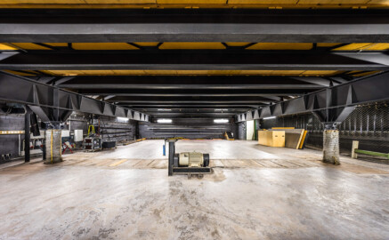 Schloss und Schlossgarten Schwetzingen - Garten - Schlosstheater - Von innen - Bühnenraum - Unterbühne - Von Westen - Blick vom westlichen Zugang nach Osten in den Raum der Unterbühne; die Neigung des Bodens der Hauptbühne (Breite x Tiefe: 15,5 x 17,0 Meter) kann von 0 bis 8 Prozent eingestellt werden; die Bühnen-Hebevorrichtung besteht aus zwei längslaufenden Doppel-T Trägern und vielen querlaufenen Trägern, auf denen der Holzboden der Bühne aufliegt, einem Elektro-Motor (in der Mitte), zwei Antriebswellen (unter der Holzabdeckung am Boden) sowie zwei Gewindespindeln zum Heben/Senken der Doppel-T Träger (in den großen Scheibenbälgen links und rechts); auf der rechten (südlichen) Seite sind die unteren Enden der vielen Züge zur Höhenverstellung der an Stahlseilen aufgehängten horizontalen Zugstangen zu sehen; rechts der Bildmitte im Hintergrund der östliche Zugang zur Unterbühne (Gesamter Bau: Länge x Breite: ca. 62 x 35 Meter; Architekt: Nicolas de Pigage (1723-1796); Bauzeit: 1752-1753, Erweiterung 1762, Sanierung: 1937, Renovierung: 1952, Generalsanierung / Umbau 1971-1974, Restaurierung: 1999-2005) (aufgenommen im September 2025, am späten Vormittag) Schloss und Schlossgarten Schwetzingen - Garten - Schlosstheater - Von innen - Bühnenraum - Unterbühne - Von Westen - Blick vom westlichen Zugang nach Osten in den Raum der Unterbühne; die Neigung des Bodens der Hauptbühne (Breite x Tiefe: 15,5 x 17,0 Meter) kann von 0 bis 8 Prozent eingestellt werden; die Bühnen-Hebevorrichtung besteht aus zwei längslaufenden Doppel-T Trägern und vielen querlaufenen Trägern, auf denen der Holzboden der Bühne aufliegt, einem Elektro-Motor (in der Mitte), zwei Antriebswellen (unter der Holzabdeckung am Boden) sowie zwei Gewindespindeln zum Heben/Senken der Doppel-T Träger (in den großen Scheibenbälgen links und rechts); auf der rechten (südlichen) Seite sind die unteren Enden der vielen Züge zur Höhenverstellung der an Stahlseilen aufgehängten horizontalen Zugstangen zu sehen; rechts der Bildmitte im Hintergrund der östliche Zugang zur Unterbühne (Gesamter Bau: Länge x Breite: ca. 62 x 35 Meter; Architekt: Nicolas de Pigage (1723-1796); Bauzeit: 1752-1753, Erweiterung 1762, Sanierung: 1937, Renovierung: 1952, Generalsanierung / Umbau 1971-1974, Restaurierung: 1999-2005) (aufgenommen im September 2025, am späten Vormittag)