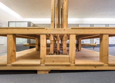 Schloss und Schlossgarten Schwetzingen - Garten - Schlosstheater - Von innen - 2. Obergeschoss (Rang), nördliches Foyer - Von Süden - Blick auf das Modell einer barocken Kulissenbühne aus Sicht einer Seitenbühne; eine solche Kulissenbühne ist in Gassen eingeteilt, die von versetzt hintereinander angeordneten, meist bemalten Seitenkulissen gebildet werden; sie ermöglichen Auftritte von den Seiten und verbergen die Beleuchtung; die Seitenkulissen sind an vertikalen Hölzern befestigt, diese sind wiederum in der Unterbühne auf einem beweglichen horizontalen Schlitten, dem sog. Kulissenwagen, montiert; jeder Wagen ist mittels Schnurzügen mit einer zentralen Walze, dem sog. Wellenbaum, verbunden; dreht man den Wellenbaum, so können gleichzeitig mehrere Kulissenwagen verschoben werden; der Zuschauer sieht dadurch das gleichzeitige Erscheinen bzw. Verschwinden mehrerer Seitenkulissen (Gesamter Bau: Länge x Breite: ca. 62 x 35 Meter; Architekt: Nicolas de Pigage (1723-1796); Bauzeit: 1752-1753, Erweiterung 1762, Sanierung: 1937, Renovierung: 1952, Generalsanierung / Umbau 1971-1974, Restaurierung: 1999-2005) (aufgenommen im September 2025, am frühen Nachmittag) Schloss und Schlossgarten Schwetzingen - Garten - Schlosstheater - Von innen - 2. Obergeschoss (Rang), nördliches Foyer - Von Süden - Blick auf das Modell einer barocken Kulissenbühne aus Sicht einer Seitenbühne; eine solche Kulissenbühne ist in Gassen eingeteilt, die von versetzt hintereinander angeordneten, meist bemalten Seitenkulissen gebildet werden; sie ermöglichen Auftritte von den Seiten und verbergen die Beleuchtung; die Seitenkulissen sind an vertikalen Hölzern befestigt, diese sind wiederum in der Unterbühne auf einem beweglichen horizontalen Schlitten, dem sog. Kulissenwagen, montiert; jeder Wagen ist mittels Schnurzügen mit einer zentralen Walze, dem sog. Wellenbaum, verbunden; dreht man den Wellenbaum, so können gleichzeitig mehrere Kulissenwagen verschoben werden; der Zuschauer sieht dadurch das gleichzeitige Erscheinen bzw. Verschwinden mehrerer Seitenkulissen (Gesamter Bau: Länge x Breite: ca. 62 x 35 Meter; Architekt: Nicolas de Pigage (1723-1796); Bauzeit: 1752-1753, Erweiterung 1762, Sanierung: 1937, Renovierung: 1952, Generalsanierung / Umbau 1971-1974, Restaurierung: 1999-2005) (aufgenommen im September 2025, am frühen Nachmittag)