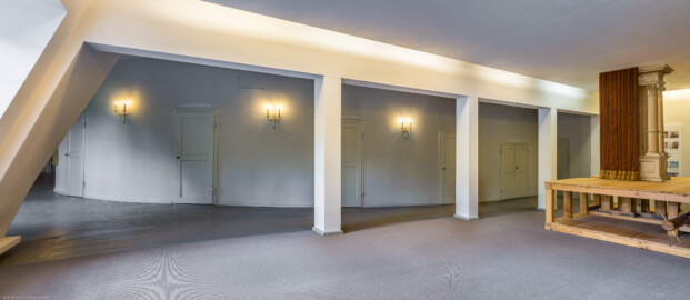 Schloss und Schlossgarten Schwetzingen - Garten - Schlosstheater - Von innen - 2. Obergeschoss (Rang), nördliches Foyer - Von Nordost - Blick nach Südwest in das nördliche Foyer im 2. Obergeschoss;  urprünglich befand sich die nördliche Mauer des Theaters an der Stelle, an der heute die drei Pfeiler stehen; in den 1950/1960er Jahren und vor allem beim großen Umbau 1971-1974 wurde das Schlosstheater nach Norden hin erweitert; originaler Bau und Anbau erkennbar am Boden: Holzboden bedeutet originaler Bau, Teppichboden bedeutet Anbau des 20. Jahrhunderts; hinter dem Durchgang auf der linken (östlichen) Seite liegt das östliche Foyer; mittig die Zugänge zu den Rängen; rechts ein Modell einer barocken Kulissenbühne (mit verschiebbaren Kulissen) (Gesamter Bau: Länge x Breite: ca. 62 x 35 Meter; Architekt: Nicolas de Pigage (1723-1796); Bauzeit: 1752-1753, Erweiterung 1762, Sanierung: 1937, Renovierung: 1952, Generalsanierung / Umbau 1971-1974, Restaurierung: 1999-2005) (aufgenommen im September 2025, am frühen Nachmittag)