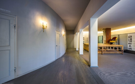 Schloss und Schlossgarten Schwetzingen - Garten - Schlosstheater - Von innen - 2. Obergeschoss (Rang), nördliches Foyer - Von Südost - Blick nach Nordwest in das nördliche Foyer im 2. Obergeschoss; urprünglich befand sich die nördliche Mauer des Theaters an der Stelle, an der heute die drei Pfeiler stehen; in den 1950/1960er Jahren und vor allem beim großen Umbau 1971-1974 wurde das Schlosstheater nach Norden hin erweitert; originaler Bau und Anbau erkennbar am Boden: Holzboden bedeutet originaler Bau, Teppichboden bedeutet Anbau des 20. Jahrhunderts; links die Zugänge zu den Rängen; rechts ein Modell einer barocken Kulissenbühne (mit verschiebbaren Kulissen) (Gesamter Bau: Länge x Breite: ca. 62 x 35 Meter; Architekt: Nicolas de Pigage (1723-1796); Bauzeit: 1752-1753, Erweiterung 1762, Sanierung: 1937, Renovierung: 1952, Generalsanierung / Umbau 1971-1974, Restaurierung: 1999-2005) (aufgenommen im September 2025, am Nachmittag) Schloss und Schlossgarten Schwetzingen - Garten - Schlosstheater - Von innen - 2. Obergeschoss (Rang), nördliches Foyer - Von Südost - Blick nach Nordwest in das nördliche Foyer im 2. Obergeschoss; urprünglich befand sich die nördliche Mauer des Theaters an der Stelle, an der heute die drei Pfeiler stehen; in den 1950/1960er Jahren und vor allem beim großen Umbau 1971-1974 wurde das Schlosstheater nach Norden hin erweitert; originaler Bau und Anbau erkennbar am Boden: Holzboden bedeutet originaler Bau, Teppichboden bedeutet Anbau des 20. Jahrhunderts; links die Zugänge zu den Rängen; rechts ein Modell einer barocken Kulissenbühne (mit verschiebbaren Kulissen) (Gesamter Bau: Länge x Breite: ca. 62 x 35 Meter; Architekt: Nicolas de Pigage (1723-1796); Bauzeit: 1752-1753, Erweiterung 1762, Sanierung: 1937, Renovierung: 1952, Generalsanierung / Umbau 1971-1974, Restaurierung: 1999-2005) (aufgenommen im September 2025, am Nachmittag)