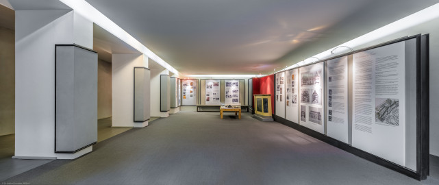 Schloss und Schlossgarten Schwetzingen - Garten - Schlosstheater - Von innen - Erdgeschoss, nördliches Foyer - Von Osten - Blick nach Westen in das nördliche Foyer im Erdgeschoss; urprünglich befand sich die nördliche Mauer des Theaters an der Stelle, an der heute die drei Pfeiler stehen; in den 1950/1960er Jahren und vor allem beim großen Umbau 1971-1974 wurde das Schlosstheater nach Norden hin erweitert; originaler Bau und Anbau erkennbar am Boden: Holzboden bedeutet originaler Bau, Teppichboden bedeutet Anbau des 20. Jahrhunderts; hinten und rechts Tafeln einer Ausstellung zur Geschichte des Theaters; rechts unterhalb der Bildmitte eine Vitrine mit Kulturmüllfunden, geborgen aus z.B. Hohlräumen oder Dachfußbereichen während der sanierungsbegleitenden bauhistorischen Untersuchung des Schwetzinger Hoftheaters durch Robert Erb und Peter Knoch, 1999-2005; rechts der Vitrine ein Nachbau eines Teils der historischen Brüstung zwischen dem Parterre und dem Orchesterraum (Gesamter Bau: Länge x Breite: ca. 62 x 35 Meter; Architekt: Nicolas de Pigage (1723-1796); Bauzeit: 1752-1753, Erweiterung 1762, Sanierung: 1937, Renovierung: 1952, Generalsanierung / Umbau 1971-1974, Restaurierung: 1999-2005) (aufgenommen im September 2025, am späten Vormittag) Schloss und Schlossgarten Schwetzingen - Garten - Schlosstheater - Von innen - Erdgeschoss, nördliches Foyer - Von Osten - Blick nach Westen in das nördliche Foyer im Erdgeschoss; urprünglich befand sich die nördliche Mauer des Theaters an der Stelle, an der heute die drei Pfeiler stehen; in den 1950/1960er Jahren und vor allem beim großen Umbau 1971-1974 wurde das Schlosstheater nach Norden hin erweitert; originaler Bau und Anbau erkennbar am Boden: Holzboden bedeutet originaler Bau, Teppichboden bedeutet Anbau des 20. Jahrhunderts; hinten und rechts Tafeln einer Ausstellung zur Geschichte des Theaters; rechts unterhalb der Bildmitte eine Vitrine mit Kulturmüllfunden, geborgen aus z.B. Hohlräumen oder Dachfußbereichen während der sanierungsbegleitenden bauhistorischen Untersuchung des Schwetzinger Hoftheaters durch Robert Erb und Peter Knoch, 1999-2005; rechts der Vitrine ein Nachbau eines Teils der historischen Brüstung zwischen dem Parterre und dem Orchesterraum (Gesamter Bau: Länge x Breite: ca. 62 x 35 Meter; Architekt: Nicolas de Pigage (1723-1796); Bauzeit: 1752-1753, Erweiterung 1762, Sanierung: 1937, Renovierung: 1952, Generalsanierung / Umbau 1971-1974, Restaurierung: 1999-2005) (aufgenommen im September 2025, am späten Vormittag)
