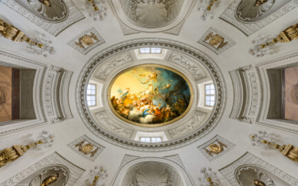 Schloss und Schlossgarten Schwetzingen - Garten - Badhaus - Von innen - Ovalsaal - Deckengemälde - Von unten - Blick nach oben in den Ovalsaal, den Tambour und auf das Deckengemälde "Aurora vertreibt die Nacht"; links ist Osten, rechts Westen, unten ist Süden (der Haupteingang); zum Gemälde: links Aurora (Göttin der Morgenröte, mit blauem Mantel, auf goldenem Wagen, von zwei weißen Sonnenpferden gezogen), darüber schwebende Putti mit Rosenkränzen, links darunter Uranus (Gott des Himmels und Urahn der Götter, versucht Aurora zurück zu halten), links ganz unten zwei spielende Putti mit Jagdhorn, unterhalb Bildmitte Tauschwestern (auf Wolkenbank, aus goldenen Gefäßen den Tau spendend), rechts etwas oberhalb der Bildmitte der Morgenstern (mit Fackel, Aurora den Weg zeigend), ganz rechts eine Eule (als Nachtvogel, den Weg zeigend) und Fledermäuse, links davon Nox (die mohnbekrönte Göttin der Nacht) (Maler: Nicolas Guibal (1725-1784); Datierung: 1772; Signaturen: links unten "N. Guibal Lotharingus inv et fecit 1772" und rechts unten "N. Guibal Lotharingus invenit et pinxit 1772"; Öl auf Leinwand, mit vergoldeten Eichenlaubkranz eingefasst;  Restaurierungen: 1890, 1949, 2006) (Gesamter Bau: Länge x Breite ca. 18 x 14 Meter, Höhe ca. 10 Meter; Architekt: Nicolas de Pigage (1723-1796); Bauzeit: 1768-1772; Gesamtinstandsetzung innen und außen: 1999-2006) (aufgenommen im Oktober 2025, am frühen Nachmittag)