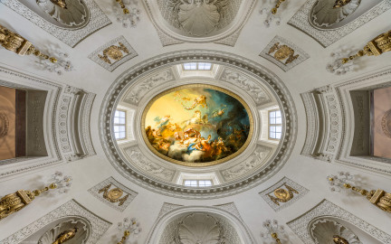 Schloss und Schlossgarten Schwetzingen - Garten - Badhaus - Von innen - Ovalsaal - Deckengemälde - Von unten - Blick nach oben in den Ovalsaal, den Tambour und auf das Deckengemälde "Aurora vertreibt die Nacht"; links ist Osten, rechts Westen, unten ist Süden (der Haupteingang); zum Gemälde: links Aurora (Göttin der Morgenröte, mit blauem Mantel, auf goldenem Wagen, von zwei weißen Sonnenpferden gezogen), darüber schwebende Putti mit Rosenkränzen, links darunter Uranus (Gott des Himmels und Urahn der Götter, versucht Aurora zurück zu halten), links ganz unten zwei spielende Putti mit Jagdhorn, unterhalb Bildmitte Tauschwestern (auf Wolkenbank, aus goldenen Gefäßen den Tau spendend), rechts etwas oberhalb der Bildmitte der Morgenstern (mit Fackel, Aurora den Weg zeigend), ganz rechts eine Eule (als Nachtvogel, den Weg zeigend) und Fledermäuse, links davon Nox (die mohnbekrönte Göttin der Nacht) (Maler: Nicolas Guibal (1725-1784); Datierung: 1772; Signaturen: links unten "N. Guibal Lotharingus inv et fecit 1772" und rechts unten "N. Guibal Lotharingus invenit et pinxit 1772"; Öl auf Leinwand, mit vergoldeten Eichenlaubkranz eingefasst; Restaurierungen: 1890, 1949, 2006) (Gesamter Bau: Länge x Breite ca. 18 x 14 Meter, Höhe ca. 10 Meter; Architekt: Nicolas de Pigage (1723-1796); Bauzeit: 1768-1772; Gesamtinstandsetzung innen und außen: 1999-2006) (aufgenommen im Oktober 2025, am frühen Nachmittag) Schloss und Schlossgarten Schwetzingen - Garten - Badhaus - Von innen - Ovalsaal - Deckengemälde - Von unten - Blick nach oben in den Ovalsaal, den Tambour und auf das Deckengemälde "Aurora vertreibt die Nacht"; links ist Osten, rechts Westen, unten ist Süden (der Haupteingang); zum Gemälde: links Aurora (Göttin der Morgenröte, mit blauem Mantel, auf goldenem Wagen, von zwei weißen Sonnenpferden gezogen), darüber schwebende Putti mit Rosenkränzen, links darunter Uranus (Gott des Himmels und Urahn der Götter, versucht Aurora zurück zu halten), links ganz unten zwei spielende Putti mit Jagdhorn, unterhalb Bildmitte Tauschwestern (auf Wolkenbank, aus goldenen Gefäßen den Tau spendend), rechts etwas oberhalb der Bildmitte der Morgenstern (mit Fackel, Aurora den Weg zeigend), ganz rechts eine Eule (als Nachtvogel, den Weg zeigend) und Fledermäuse, links davon Nox (die mohnbekrönte Göttin der Nacht) (Maler: Nicolas Guibal (1725-1784); Datierung: 1772; Signaturen: links unten "N. Guibal Lotharingus inv et fecit 1772" und rechts unten "N. Guibal Lotharingus invenit et pinxit 1772"; Öl auf Leinwand, mit vergoldeten Eichenlaubkranz eingefasst; Restaurierungen: 1890, 1949, 2006) (Gesamter Bau: Länge x Breite ca. 18 x 14 Meter, Höhe ca. 10 Meter; Architekt: Nicolas de Pigage (1723-1796); Bauzeit: 1768-1772; Gesamtinstandsetzung innen und außen: 1999-2006) (aufgenommen im Oktober 2025, am frühen Nachmittag)
