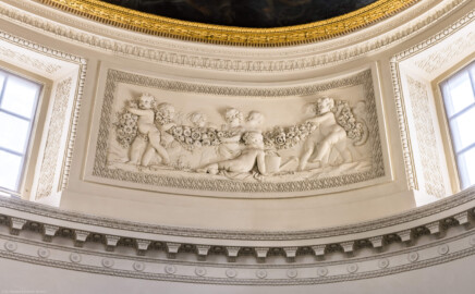 Schloss und Schlossgarten Schwetzingen - Garten - Badhaus - Von innen - Ovalsaal - Puttenfriese - Von Nordost - Südwestliches Feld im Tambour: neun spielende Putti, verbunden durch eine Blumen- und Fruchtgirlande, ein Putto mit Gießkanne, eingebettet in ein Feld mit Tropfenstuck, umgeben von einem glatten Rahmen (Stuckateur: Giuseppe Antonio Pozzi (1732–1811)) (Gesamter Bau: Länge x Breite ca. 18 x 14 Meter, Höhe ca. 10 Meter; Architekt: Nicolas de Pigage (1723-1796); Bauzeit: 1768-1772; Gesamtinstandsetzung innen und außen: 1999-2006) (aufgenommen im Oktober 2025, am frühen Nachmittag)