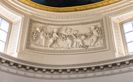 Schloss und Schlossgarten Schwetzingen - Garten - Badhaus - Von innen - Ovalsaal - Puttenfriese - Von Südost - Nordwestliches Feld im Tambour: acht spielende Putti, verbunden durch eine Blumen- und Fruchtgirlande, eingebettet in ein Feld mit Tropfenstuck, umgeben von einem glatten Rahmen (Stuckateur: Giuseppe Antonio Pozzi (1732–1811)) (Gesamter Bau: Länge x Breite ca. 18 x 14 Meter, Höhe ca. 10 Meter; Architekt: Nicolas de Pigage (1723-1796); Bauzeit: 1768-1772; Gesamtinstandsetzung innen und außen: 1999-2006) (aufgenommen im Oktober 2025, am frühen Nachmittag) Schloss und Schlossgarten Schwetzingen - Garten - Badhaus - Von innen - Ovalsaal - Puttenfriese - Von Südost - Nordwestliches Feld im Tambour: acht spielende Putti, verbunden durch eine Blumen- und Fruchtgirlande, eingebettet in ein Feld mit Tropfenstuck, umgeben von einem glatten Rahmen (Stuckateur: Giuseppe Antonio Pozzi (1732–1811)) (Gesamter Bau: Länge x Breite ca. 18 x 14 Meter, Höhe ca. 10 Meter; Architekt: Nicolas de Pigage (1723-1796); Bauzeit: 1768-1772; Gesamtinstandsetzung innen und außen: 1999-2006) (aufgenommen im Oktober 2025, am frühen Nachmittag)