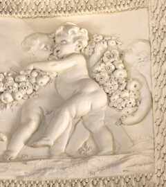 Schloss und Schlossgarten Schwetzingen - Garten - Badhaus - Von innen - Ovalsaal - Puttenfriese - Von Nordost - Ausschnitt aus dem südwestliches Feld im Tambour: spielende Putti, verbunden durch eine Blumen- und Fruchtgirlande (Stuckateur: Giuseppe Antonio Pozzi (1732–1811)) (Gesamter Bau: Länge x Breite ca. 18 x 14 Meter, Höhe ca. 10 Meter; Architekt: Nicolas de Pigage (1723-1796); Bauzeit: 1768-1772; Gesamtinstandsetzung innen und außen: 1999-2006) (aufgenommen im Oktober 2025, am frühen Nachmittag)