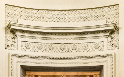 Schloss und Schlossgarten Schwetzingen - Garten - Badhaus - Von innen - Ovalsaal - Östlicher Durchgang - Von Westen - Blick von der Mitte des Ovalsaals nach Osten auf die Verdachung des Durchgangs in das östliche Vorzimmer; Verdachung der ionischen Ordnung, mit Tropfenstuck, Perlstab, Eierstab, Akanthusblättern, Scheiben mit Rosetten; links und rechts bärtige Masken in Form von Halbmonden (Stuckateur: Giuseppe Antonio Pozzi (1732–1811) zugeschrieben) (Gesamter Bau: Länge x Breite ca. 18 x 14 Meter, Höhe ca. 10 Meter; Architekt: Nicolas de Pigage (1723-1796); Bauzeit: 1768-1772; Gesamtinstandsetzung innen und außen: 1999-2006) (aufgenommen im Oktober 2025, am Nachmittag) Schloss und Schlossgarten Schwetzingen - Garten - Badhaus - Von innen - Ovalsaal - Östlicher Durchgang - Von Westen - Blick von der Mitte des Ovalsaals nach Osten auf die Verdachung des Durchgangs in das östliche Vorzimmer; Verdachung der ionischen Ordnung, mit Tropfenstuck, Perlstab, Eierstab, Akanthusblättern, Scheiben mit Rosetten; links und rechts bärtige Masken in Form von Halbmonden (Stuckateur: Giuseppe Antonio Pozzi (1732–1811) zugeschrieben) (Gesamter Bau: Länge x Breite ca. 18 x 14 Meter, Höhe ca. 10 Meter; Architekt: Nicolas de Pigage (1723-1796); Bauzeit: 1768-1772; Gesamtinstandsetzung innen und außen: 1999-2006) (aufgenommen im Oktober 2025, am Nachmittag)