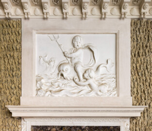 Schloss und Schlossgarten Schwetzingen - Garten - Badhaus - Von innen - Baderaum - Supraporte, Nordseite - Von Süden - Blick auf die Supraporte über der (nördlichen) Ausgangstür; Putti mit Wasserattributen in Reliefdarstellung, umgeben von einem glatten Rahmen; ein Putto reitet einen Delphin und hält ein Dreizack in der Hand, ein zweiter Putto schwimmt in stark bewegten Wellen auf den Delphin zu und hält eine kleine Muschel in seiner Hand, ein dritter Putto im Hintergrund bläst ein Muschelhorn; Gesims der Türeinfassung aus Stuck geschmückt mit Perlstab und Blattfries; in der Kehle der Decke Stuckkonsolen mit birnenförmigen Tropfen, Muscheln, Blütenrosetten (Stuckateur: Giuseppe Antonio Pozzi (1732–1811)) (Gesamter Bau: Länge x Breite ca. 18 x 14 Meter, Höhe ca. 10 Meter; Architekt: Nicolas de Pigage (1723-1796); Bauzeit: 1768-1772; Gesamtinstandsetzung innen und außen: 1999-2006) (aufgenommen im Oktober 2025, am Nachmittag)