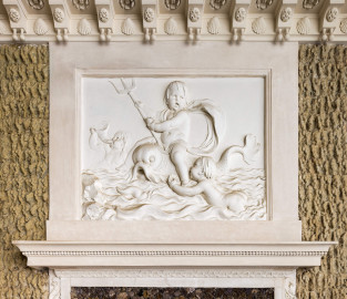 Schloss und Schlossgarten Schwetzingen - Garten - Badhaus - Von innen - Baderaum - Supraporte, Nordseite - Von Süden - Blick auf die Supraporte über der (nördlichen) Ausgangstür; Putti mit Wasserattributen in Reliefdarstellung, umgeben von einem glatten Rahmen; ein Putto reitet einen Delphin und hält ein Dreizack in der Hand, ein zweiter Putto schwimmt in stark bewegten Wellen auf den Delphin zu und hält eine kleine Muschel in seiner Hand, ein dritter Putto im Hintergrund bläst ein Muschelhorn; Gesims der Türeinfassung aus Stuck geschmückt mit Perlstab und Blattfries; in der Kehle der Decke Stuckkonsolen mit birnenförmigen Tropfen, Muscheln, Blütenrosetten (Stuckateur: Giuseppe Antonio Pozzi (1732–1811)) (Gesamter Bau: Länge x Breite ca. 18 x 14 Meter, Höhe ca. 10 Meter; Architekt: Nicolas de Pigage (1723-1796); Bauzeit: 1768-1772; Gesamtinstandsetzung innen und außen: 1999-2006) (aufgenommen im Oktober 2025, am Nachmittag) Schloss und Schlossgarten Schwetzingen - Garten - Badhaus - Von innen - Baderaum - Supraporte, Nordseite - Von Süden - Blick auf die Supraporte über der (nördlichen) Ausgangstür; Putti mit Wasserattributen in Reliefdarstellung, umgeben von einem glatten Rahmen; ein Putto reitet einen Delphin und hält ein Dreizack in der Hand, ein zweiter Putto schwimmt in stark bewegten Wellen auf den Delphin zu und hält eine kleine Muschel in seiner Hand, ein dritter Putto im Hintergrund bläst ein Muschelhorn; Gesims der Türeinfassung aus Stuck geschmückt mit Perlstab und Blattfries; in der Kehle der Decke Stuckkonsolen mit birnenförmigen Tropfen, Muscheln, Blütenrosetten (Stuckateur: Giuseppe Antonio Pozzi (1732–1811)) (Gesamter Bau: Länge x Breite ca. 18 x 14 Meter, Höhe ca. 10 Meter; Architekt: Nicolas de Pigage (1723-1796); Bauzeit: 1768-1772; Gesamtinstandsetzung innen und außen: 1999-2006) (aufgenommen im Oktober 2025, am Nachmittag)