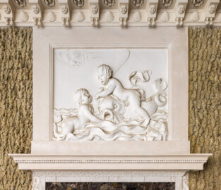 Schloss und Schlossgarten Schwetzingen - Garten - Badhaus - Von innen - Baderaum - Supraporte, Südseite - Von Norden - Blick auf die Supraporte über der (südlichen) Eingangstür; Putti mit Wasserattributen in Reliefdarstellung, umgeben von einem glatten Rahmen; ein Putto reitet einen Delphin und hält ein Paddel in der Hand, ein zweiter Putto schwimmt in stark bewegten Wellen; Gesims der Türeinfassung aus Stuck geschmückt mit Perlstab und Blattfries; in der Kehle der Decke Stuckkonsolen mit birnenförmigen Tropfen, Muscheln, Blütenrosetten (Stuckateur: Giuseppe Antonio Pozzi (1732–1811)) (Gesamter Bau: Länge x Breite ca. 18 x 14 Meter, Höhe ca. 10 Meter; Architekt: Nicolas de Pigage (1723-1796); Bauzeit: 1768-1772; Gesamtinstandsetzung innen und außen: 1999-2006) (aufgenommen im Oktober 2025, am Nachmittag)