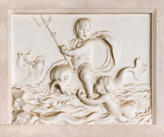 Schloss und Schlossgarten Schwetzingen - Garten - Badhaus - Von innen - Baderaum - Supraporte, Nordseite - Von Süden - Putti mit Wasserattributen in Reliefdarstellung; ein Putto reitet einen Delphin und hält ein Dreizack in der Hand, ein zweiter Putto schwimmt in stark bewegten Wellen auf den Delphin zu und hält eine kleine Muschel in seiner Hand, ein dritter Putto im Hintergrund bläst ein Muschelhorn (Stuckateur: Giuseppe Antonio Pozzi (1732–1811)) (Gesamter Bau: Länge x Breite ca. 18 x 14 Meter, Höhe ca. 10 Meter; Architekt: Nicolas de Pigage (1723-1796); Bauzeit: 1768-1772; Gesamtinstandsetzung innen und außen: 1999-2006) (aufgenommen im Oktober 2025, am Nachmittag)
