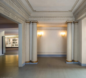 Schloss und Schlossgarten Schwetzingen - Garten - Schlosstheater - Von innen - Erdgeschoss, östliches Foyer - Von Süden - Blick nach Norden auf das nördliche Ende des östlichen Foyers; links der Zugang zum nördlichen Foyer (mit einer Ausstellung zur Geschichte des Theaters), rechts (nicht sichtbar) eine Notausgangstür (Gesamter Bau: Länge x Breite: ca. 62 x 35 Meter; Architekt: Nicolas de Pigage (1723-1796); Bauzeit: 1752-1753, Erweiterung 1762, Sanierung: 1937, Renovierung: 1952, Generalsanierung / Umbau 1971-1974, Restaurierung: 1999-2005) (aufgenommen im Oktober 2025, am frühen Nachmittag)
