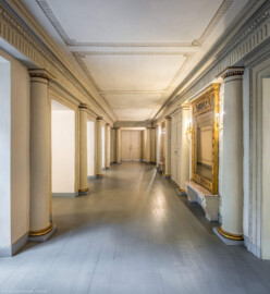 Schloss und Schlossgarten Schwetzingen - Garten - Schlosstheater - Von innen - Erdgeschoss, östliches Foyer - Von Norden - Blick vom nördlichen Ende des Gangs im östlichen Foyer nach Süden; ganz links eine (nicht sichtbare) Notausgangstür, links die drei Durchgänge zum ehemaligen Vestibül (im ehemaligen zentralen östlichen Treppenhaus), im Hintergrund in der Bildmitte der zentrale (hier geschlossene) Eingang zum Parkett des Theaters, rechts davon (nicht sichtbar) der Zugang zum südlichen Foyer, rechts davon die zentrale Eingangstür zum Parkett (umgeben von zwei Spiegeln) und ganz rechts der Zugang zum nördlichen Foyer (Gesamter Bau: Länge x Breite: ca. 62 x 35 Meter; Architekt: Nicolas de Pigage (1723-1796); Bauzeit: 1752-1753, Erweiterung 1762, Sanierung: 1937, Renovierung: 1952, Generalsanierung / Umbau 1971-1974, Restaurierung: 1999-2005) (aufgenommen im Oktober 2025, am Nachmittag)