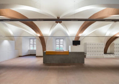 Schloss und Schlossgarten Schwetzingen - Schloss - Mittelbau - Von innen - Erdgeschoss, Nordseite - Besucherzentrum / ehemaliger Hochkeller - Von Süden - Blick vom westlichen Eingang in der Vorhalle nach Norden in den gewölbten Raum; im 16. Jahrhundert diente der Raum als Hofstube (eine Art Mensa), später als Hochkeller, ab 2016 als Besucherzentrum; der Boden des Raum lag früher 4 Treppenstufen tiefer, der Raum besaß Zwischenwände, ein Gewölbeschlusstein trägt die Jahreszahl 1527 (Raum: Länge x Breite: ca. 16 x 6 Meter, Höhe (bis Schlussstein): ca. 3,5 Meter; 4 Joche, 3 Gurtbögen, 3 Kreuzrippengewölbe, ein Kreuzgratgewölbe im Osten; Nordwand: 2 Fenster, 2 vermauerte Öffnungen, Standerker: 1 kleines Fenster, Südwand: 3 Türen, Westwand: verschlossene Durchgangstür) (Mittelbau: Länge Westseite ca. 45 Meter, Breite Süd-/Nordseite ca. 38 Meter; Wiederaufbau / Erweiterung: 1698-1717; Architekt: Johann Adam Breunig) (aufgenommen im November 2025, am frühen Nachmittag)