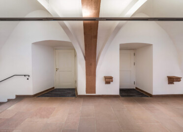 Schloss und Schlossgarten Schwetzingen - Schloss - Mittelbau - Von innen - Erdgeschoss, Nordseite - Besucherzentrum / ehemaliger Hochkeller - Von Norden - Blick von der Mitte des Raums unterhalb des 2. Gurtbogens von Osten nach Süden in den gewölbten Raum und auf die beiden Türen zur Vorhalle; im 16. Jahrhundert diente der Raum als Hofstube (eine Art Mensa), später als Hochkeller, ab 2016 als Besucherzentrum; der Boden des Raum lag früher 4 Treppenstufen tiefer, der Raum besaß Zwischenwände, ein Gewölbeschlusstein trägt die Jahreszahl 1527 (Raum: Länge x Breite: ca. 16 x 6 Meter, Höhe (bis Schlussstein): ca. 3,5 Meter; 4 Joche, 3 Gurtbögen, 3 Kreuzrippengewölbe, ein Kreuzgratgewölbe im Osten; Nordwand: 2 Fenster, 2 vermauerte Öffnungen, Standerker: 1 kleines Fenster, Südwand: 3 Türen, Westwand: verschlossene Durchgangstür) (Mittelbau: Länge Westseite ca. 45 Meter, Breite Süd-/Nordseite ca. 38 Meter; Wiederaufbau / Erweiterung: 1698-1717; Architekt: Johann Adam Breunig) (aufgenommen im November 2025, am späten Vormittag) Schloss und Schlossgarten Schwetzingen - Schloss - Mittelbau - Von innen - Erdgeschoss, Nordseite - Besucherzentrum / ehemaliger Hochkeller - Von Norden - Blick von der Mitte des Raums unterhalb des 2. Gurtbogens von Osten nach Süden in den gewölbten Raum und auf die beiden Türen zur Vorhalle; im 16. Jahrhundert diente der Raum als Hofstube (eine Art Mensa), später als Hochkeller, ab 2016 als Besucherzentrum; der Boden des Raum lag früher 4 Treppenstufen tiefer, der Raum besaß Zwischenwände, ein Gewölbeschlusstein trägt die Jahreszahl 1527 (Raum: Länge x Breite: ca. 16 x 6 Meter, Höhe (bis Schlussstein): ca. 3,5 Meter; 4 Joche, 3 Gurtbögen, 3 Kreuzrippengewölbe, ein Kreuzgratgewölbe im Osten; Nordwand: 2 Fenster, 2 vermauerte Öffnungen, Standerker: 1 kleines Fenster, Südwand: 3 Türen, Westwand: verschlossene Durchgangstür) (Mittelbau: Länge Westseite ca. 45 Meter, Breite Süd-/Nordseite ca. 38 Meter; Wiederaufbau / Erweiterung: 1698-1717; Architekt: Johann Adam Breunig) (aufgenommen im November 2025, am späten Vormittag)