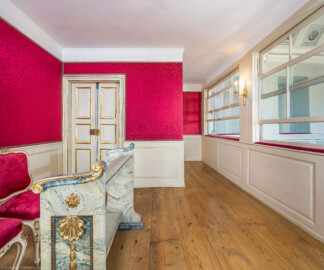 Schloss und Schlossgarten Schwetzingen - Schloss - Nordflügel, Nord-Süd-Teil - Schlosskapelle - Hofloge - Von Osten - Blick in die Hofloge des Kurfürstenpaars Carl Theodor (1724-1799, reg. 1742-1799) und Elisabeth Auguste (1721-1794) sowie auf einen Betstuhl und Stühle; links und links am Ende des Gangs (nicht sichtbar) die Türen zum ersten Vorzimmer des Kurfürsten (Schlosskapelle: Länge ca. 14 Meter, Breite ca. 10 Meter, Höhe: bis unter das Dach, Achsen: 6, Eingang: Ostseite; Bauzeit: zwischen 1698 und 1715; Architekten: Johann Adam Breunig, Simon Sarto; Umbau innen im klassizistischen Stil: 1804-1806, Architekt: Friedrich Weinbrenner) (aufgenommen im Dezember 2025, um die Mittagszeit) Schloss und Schlossgarten Schwetzingen - Schloss - Nordflügel, Nord-Süd-Teil - Schlosskapelle - Hofloge - Von Osten - Blick in die Hofloge des Kurfürstenpaars Carl Theodor (1724-1799, reg. 1742-1799) und Elisabeth Auguste (1721-1794) sowie auf einen Betstuhl und Stühle; links und links am Ende des Gangs (nicht sichtbar) die Türen zum ersten Vorzimmer des Kurfürsten (Schlosskapelle: Länge ca. 14 Meter, Breite ca. 10 Meter, Höhe: bis unter das Dach, Achsen: 6, Eingang: Ostseite; Bauzeit: zwischen 1698 und 1715; Architekten: Johann Adam Breunig, Simon Sarto; Umbau innen im klassizistischen Stil: 1804-1806, Architekt: Friedrich Weinbrenner) (aufgenommen im Dezember 2025, um die Mittagszeit)