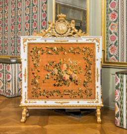 Schloss und Schlossgarten Schwetzingen - Schloss - Mittelbau - Von innen - 1. Obergeschoss - Appartment des Kurfürsten - Schlafzimmer - Südwand - Blick auf den Kaminschirm (Datierung: um 1775; Rahmen: weiß-gold gefasst, Blatt: Savonnerie mit Blumen auf braunviolettem Grund, Aufsatz: Monogramm "CT" für Carl Theodor mit zwei aufsteigenden Pfälzer Löwen) (aufgenommen im Januar 2026, am Nachmittag)