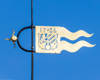 Schloss und Schlossgarten Schwetzingen - Schloss - Nordflügel / Hofkavaliersflügel - Von Süden - Blick vom Nordfenster des Raums 246 im 3. Obergeschoss des Schlossmittelbaus auf die Wetterfahne des Dachreiters in der Nordwestecke des Nordflügels; die Wetterfahne zeigt das Wappen der Kurpfalz und die Jahreszahl 1786 (NordFlügel: L-förmig, Länge x Breite Längsbau ca. 50 x 14 Meter, Querbau ca. 15 x 12 Meter; Architekt: Johann Adam Breunig (1660-1727); Fertigstellung: 1710) (aufgenommen im März 2026, am späten Vormittag)