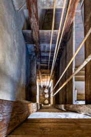 Schloss und Schlossgarten Schwetzingen - Schloss - Mittelbau - Von innen - 3. Obergeschoss - Südlicher Turm - Von oben - Blick vom Fenster nach Westen und nach unten in den holzverkleideten Seilschacht des südlichen Turms; drei kugelförmige Antriebsgewichte an drei Seilen mit Umlenkrollen im Seilschacht treiben das Uhrwerk und das Schlagwerk der alten Schlossuhr im Dachgeschoss des Turms an (Turmuhr von Johann Jacob Möllinger (1695-1763) mit Viertel- und Stundenschlag, errichtet 1763, stillgelegt 1968) (aufgenommen im März 2026, am späten Nachmittag) Schloss und Schlossgarten Schwetzingen - Schloss - Mittelbau - Von innen - 3. Obergeschoss - Südlicher Turm - Von oben - Blick vom Fenster nach Westen und nach unten in den holzverkleideten Seilschacht des südlichen Turms; drei kugelförmige Antriebsgewichte an drei Seilen mit Umlenkrollen im Seilschacht treiben das Uhrwerk und das Schlagwerk der alten Schlossuhr im Dachgeschoss des Turms an (Turmuhr von Johann Jacob Möllinger (1695-1763) mit Viertel- und Stundenschlag, errichtet 1763, stillgelegt 1968) (aufgenommen im März 2026, am späten Nachmittag)