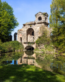 Schloss und Schlossgarten Schwetzingen - Garten - Römisches Wasserkastell - Von außen - Von Südost - Blick auf das Römische Wasserkastell; eine künstliche Ruine, teils in Tuffstein, mit zwei Türmen (westlich zwei-, östlich dreigeschossig), Mittelpartie mit großem Rundbogen, darüber eine Plattform, darunter ein Gewölbe mit Durchfluss des Leimbachs nach Norden; im östlichen Mittelgeschoss ein Tonrelief mit einer Wassernymphe von Franz Conrad Linck (1730-1793) (Kastell: Länge x Breite: ca. 15 x 8 Meter; Bauzeit: 1779-1780; Architekt: Nicolas de Pigage) (aufgenommen im April 2026, am späten Vormittag)