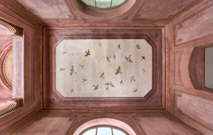Schloss und Schlossgarten Schwetzingen - Garten - Badhausanlage - Perspektiv - Westlicher Flügel - Von unten - Zentraler Blick von der Mitte der westlichen Halle nach oben auf drei Wände und die Decke; an der Decke die Illusion einer Voliere: ein Gitter, unter dem etliche fliegende Vögel zu sehen sind, darüber ein bewölkter Himmel; Decke und Wände sind mit gemalten rechteckigen Feldern gegliedert, die Ecken tragen Rosettenschmuck; links (östlich) die zentrale Halle, rechts der westliche Eingang,  (Perspektiv: Abmessungen Länge x Breite x Höhe: Laubengang ca. 40 x 3,5 x 4,5 Meter, Bau ca. 16 x 4,5 bis 11 x 6,5 Meter, Bildwand ca. 9 x 1 x 7,5 Meter; Fertigstellung: 1775, Gesamtinstandsetzung: 1988-1991, Restaurierung Laubengang: 2022; Architekt: Nicolas de Pigage) (aufgenommen im April 2026, am frühen Nachmittag)