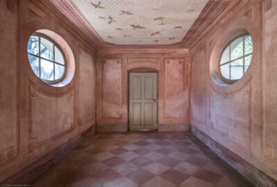 Schloss und Schlossgarten Schwetzingen - Garten - Badhausanlage - Perspektiv - Westlicher Flügel - Von Osten - Blick von der zentralen Halle in den westlichen Seitenflügel sowie auf die Rundfenster und die westliche Holztür; an der Decke die Illusion einer Voliere: ein Gitter, unter dem etliche fliegende Vögel zu sehen sind, darüber ein bewölkter Himmel; Decke und Wände sind mit gemalten rechteckigen Feldern gegliedert, die Ecken tragen Rosettenschmuck (Perspektiv: Abmessungen Länge x Breite x Höhe: Laubengang ca. 40 x 3,5 x 4,5 Meter, Bau ca. 16 x 4,5 bis 11 x 6,5 Meter, Bildwand ca. 9 x 1 x 7,5 Meter; Fertigstellung: 1775, Gesamtinstandsetzung: 1988-1991, Restaurierung Laubengang: 2022; Architekt: Nicolas de Pigage) (aufgenommen im April 2026, am Nachmittag)