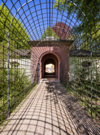Schloss und Schlossgarten Schwetzingen - Garten - Badhausanlage - Perspektiv - Von Süden - Blick vom Laubengang (Berceau de treillage) nach Norden auf den mittleren Teil der Anlage, in den zentralen Innenraum, in die Grotte und auf die gemalte Landschaft ("Das Ende der Welt") (Perspektiv: Abmessungen Länge x Breite x Höhe: Laubengang ca. 40 x 3,5 x 4,5 Meter, Bau ca. 16 x 4,5 bis 11 x 6,5 Meter, Bildwand ca. 9 x 1 x 7,5 Meter; Fertigstellung: 1775, Gesamtinstandsetzung: 1988-1991, Restaurierung Laubengang: 2022; Architekt: Nicolas de Pigage) (aufgenommen im April 2026, um die Mittagszeit)