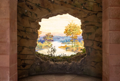 Schloss und Schlossgarten Schwetzingen - Garten - Badhausanlage - Perspektiv - Grotte / Vorgrotte / Bildwand - Von Süden - Blick von der Halle in die Grotte mit der Öffnung zur Vorgrotte und auf das Gemälde "Das Ende der Welt" an der gewölbten Bildwand; dargestellt ist eine idyllische Flusslandschaft (Rhein mit Auenlandschaft?); Fresko nach einer Vorlage von Ferdinand Kobell (1740-1799), ursprünglich gemalt von dem Mannheimer Theatermaler Truckenmüller oder dem Hofmaler Hubert Willwerth; Fresko seither mehrfach restauriert  (Perspektiv: Abmessungen Länge x Breite x Höhe: Laubengang ca. 40 x 3,5 x 4,5 Meter, Bau ca. 16 x 4,5 bis 11 x 6,5 Meter, Bildwand ca. 9 x 1 x 7,5 Meter; Fertigstellung: 1775, Gesamtinstandsetzung: 1988-1991, Restaurierung Laubengang: 2022; Architekt: Nicolas de Pigage) (aufgenommen im April 2026, am frühen Nachmittag)