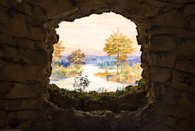Schloss und Schlossgarten Schwetzingen - Garten - Badhausanlage - Perspektiv - Grotte / Vorgrotte / Bildwand - Von Süden - Blick auf die Nordwand der Grotte mit der Öffnung zur Vorgrotte und auf das Gemälde "Das Ende der Welt" an der gewölbten Bildwand; dargestellt ist eine idyllische Flusslandschaft (Rhein mit Auenlandschaft?); Fresko nach einer Vorlage von Ferdinand Kobell (1740-1799), ursprünglich gemalt von dem Mannheimer Theatermaler Truckenmüller oder dem Hofmaler Hubert Willwerth; Fresko seither mehrfach restauriert  (Perspektiv: Abmessungen Länge x Breite x Höhe: Laubengang ca. 40 x 3,5 x 4,5 Meter, Bau ca. 16 x 4,5 bis 11 x 6,5 Meter, Bildwand ca. 9 x 1 x 7,5 Meter; Fertigstellung: 1775, Gesamtinstandsetzung: 1988-1991, Restaurierung Laubengang: 2022; Architekt: Nicolas de Pigage) (aufgenommen im April 2026, am frühen Nachmittag)