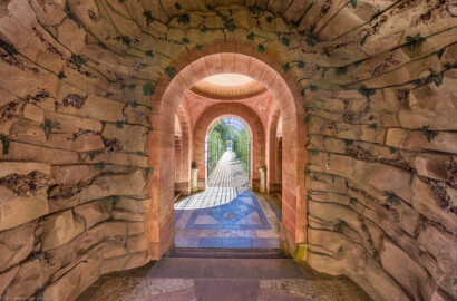 Schloss und Schlossgarten Schwetzingen - Garten - Badhausanlage - Perspektiv - Grotte / Halle - Von Norden - Blick von der Vorgrotte nach Süden in die Grotte, die Halle und in den Laubengang; die Felsengrotte ist geschmückt mit Muscheln, Algen, Halbedelsteinen und Mineralkristallen (Perspektiv: Abmessungen Länge x Breite x Höhe: Laubengang ca. 40 x 3,5 x 4,5 Meter, Bau ca. 16 x 4,5 bis 11 x 6,5 Meter, Bildwand ca. 9 x 1 x 7,5 Meter; Fertigstellung: 1775, Gesamtinstandsetzung: 1988-1991, Restaurierung Laubengang: 2022; Architekt: Nicolas de Pigage) (aufgenommen im April 2026, am Nachmittag)