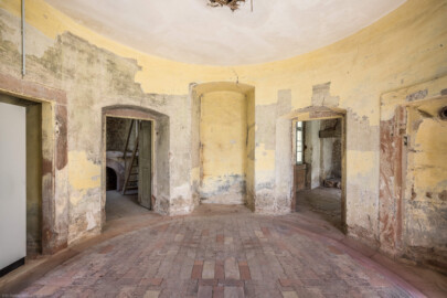 Schloss und Schlossgarten Schwetzingen - Garten - Badhausanlage - Badhausküche - Von innen - Rotunde - Von Südwest - Blick von der Eingangstür in den runden Eingangsraum; ganz links und ganz rechts Wandnischen, links die Tür zum Heizraum (mit der Empore für einen Kessel und der Holzstiege), rechts die Tür zur Küche, in der Mitte eine Wandnische (ursprünglich als zweite Außentür geplant) (Gesamter Bau: Länge x Breite (winkelförmig) ca. 13 x 11 Meter, Höhe (über Rotunde) ca. 8 Meter; Raum: Durchmesser ca. 5 Meter, Höhe ca. 3 Meter; Architekt: Nicolas de Pigage (1723-1796); Bauzeit: 1768-1772, Dachinstandsetzung: 1983-1985, Instandsetzung: 2013-2015) (aufgenommen im April 2026, am Nachmittag) Schloss und Schlossgarten Schwetzingen - Garten - Badhausanlage - Badhausküche - Von innen - Rotunde - Von Südwest - Blick von der Eingangstür in den runden Eingangsraum; ganz links und ganz rechts Wandnischen, links die Tür zum Heizraum (mit der Empore für einen Kessel und der Holzstiege), rechts die Tür zur Küche, in der Mitte eine Wandnische (ursprünglich als zweite Außentür geplant) (Gesamter Bau: Länge x Breite (winkelförmig) ca. 13 x 11 Meter, Höhe (über Rotunde) ca. 8 Meter; Raum: Durchmesser ca. 5 Meter, Höhe ca. 3 Meter; Architekt: Nicolas de Pigage (1723-1796); Bauzeit: 1768-1772, Dachinstandsetzung: 1983-1985, Instandsetzung: 2013-2015) (aufgenommen im April 2026, am Nachmittag)