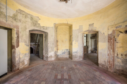 Schloss und Schlossgarten Schwetzingen - Garten - Badhausanlage - Badhausküche - Von innen - Rotunde - Von Südwest - Blick von der Eingangstür in den runden Eingangsraum; ganz links und ganz rechts Wandnischen, links die Tür zum Heizraum (mit der Empore für einen Kessel und der Holzstiege), rechts die Tür zur Küche, in der Mitte eine Wandnische (ursprünglich als zweite Außentür geplant) (Gesamter Bau: Länge x Breite (winkelförmig) ca. 13 x 11 Meter, Höhe (über Rotunde) ca. 8 Meter; Raum: Durchmesser ca. 5 Meter, Höhe ca. 3 Meter; Architekt: Nicolas de Pigage (1723-1796); Bauzeit: 1768-1772, Dachinstandsetzung: 1983-1985, Instandsetzung: 2013-2015) (aufgenommen im April 2026, am Nachmittag)
