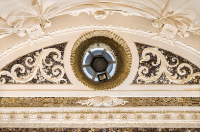Schloss und Schlossgarten Schwetzingen - Garten - Badhaus - Von innen - Baderaum - Decke - Von unten - Blick vom Wasserbecken nach oben auf die Decke der Wanne; von oben nach unten: mehrfach geraffter Stuckvorhang,  große Konsolen, daran quastenbesetzte Seile befestigt, zwischen Konsolen Stuckplastik mit Urnen und Delphin, Fries mit Muscheln, Kreissegment mit drei Feldern, mittig eine Öffnung, mit Tropfenstuck verkleidet, zu einer Laterne zur Entlüftung und Beleuchtung führend, links und rechts davon Felder mit Amethysten und Akanthusranken, darunter ein Feld mit Muscheln und Bruchsteinen, darunter Kehle mit Stuckkonsolen mit birnenförmigen Tropfen, Muscheln, Blütenrosetten und Lorbeergirlande, darunter ein Streifen Rauputz in Tropfenoptik, dunkle Fläche mit Halbedelsteinen (Stuckateur: Giuseppe Antonio Pozzi (1732–1811)) (Gesamter Bau: Länge x Breite ca. 18 x 14 Meter, Höhe ca. 10 Meter; Architekt: Nicolas de Pigage (1723-1796); Bauzeit: 1768-1772; Gesamtinstandsetzung innen und außen: 1999-2006) (aufgenommen im Mai 2026, am späten Nachmittag)