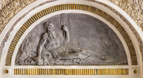 Schloss und Schlossgarten Schwetzingen - Garten - Badhausanlage - Östliches Achathäuschen - Südwand - Blick auf eine Lünette mit einem Bleirelief an der rechten Seitenwand; Darstellung eines bärtigen Flussgottes, gegen einen Felsen lehnend, umgeben von Schilfgras; rechte Hand auf Steine gestützt, mit linker Hand ein Ruder haltend; zwischen rechtem Arm und Hüft eine Urne, aus der Wasser läuft (Bildhauer: Franz Conrad Linck (1730-1793), Datierung: um 1770-1775, Material: Blei, Breite x Höhe: 125 x 58 Zentimeter) (Achathäuschen: Abmessungen Breite x Tiefe x Höhe 3,2 x 3,0 x 6,4 Meter, Innenraum Breite x Tiefe ca. 2 x 2 Meter; Architekt: Nicolas de Pigage, Fertigstellung: um 1775, Instandsetzung: 1991 - 1995) (aufgenommen im Mai 2026, am späten Vormittag)
